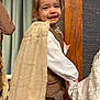 Octavie a rejoint le concours — aidez-le/la à gagner de superbes lots ! child, smiling, cape, faux_fur, white_shirt, brown_vest, holding_hands, indoor, portrait, happy, young_child, curtain, wooden_door, playing, friendship, warm_lighting, cute, face, person, costume