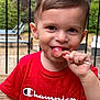 toddler, child, red_shirt, lollipop, smiling, outdoor, deck, wooden_floor, garden, patio_furniture, boy, short_hair, daylight, happy, cute, person, portrait, summer, playful, casual_clothing