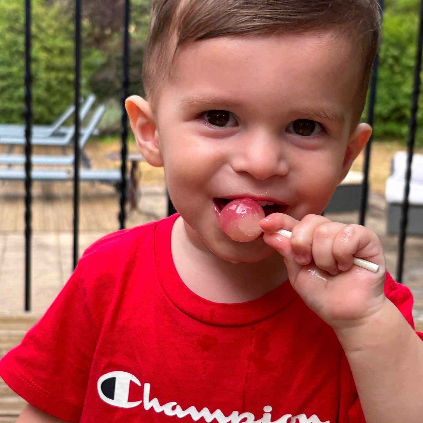 Soan participe au concours pour gagner de l'argent avec cette photo : boy, casual_clothing, child, cute, daylight, deck, garden, happy, lollipop, outdoor, patio_furniture, person, playful, portrait, red_shirt, short_hair, smiling, summer, toddler, wooden_floor