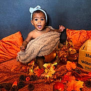 Trelawny is registered to the contest to win money with this photo: autumn_leaves, baby, blanket, child, cozy, cute, decorations, fall_decor, festive, happy, headband, indoor, orange_pillows, pinecones, portrait, pumpkin, seasonal, sitting, smiling, wooden_box
