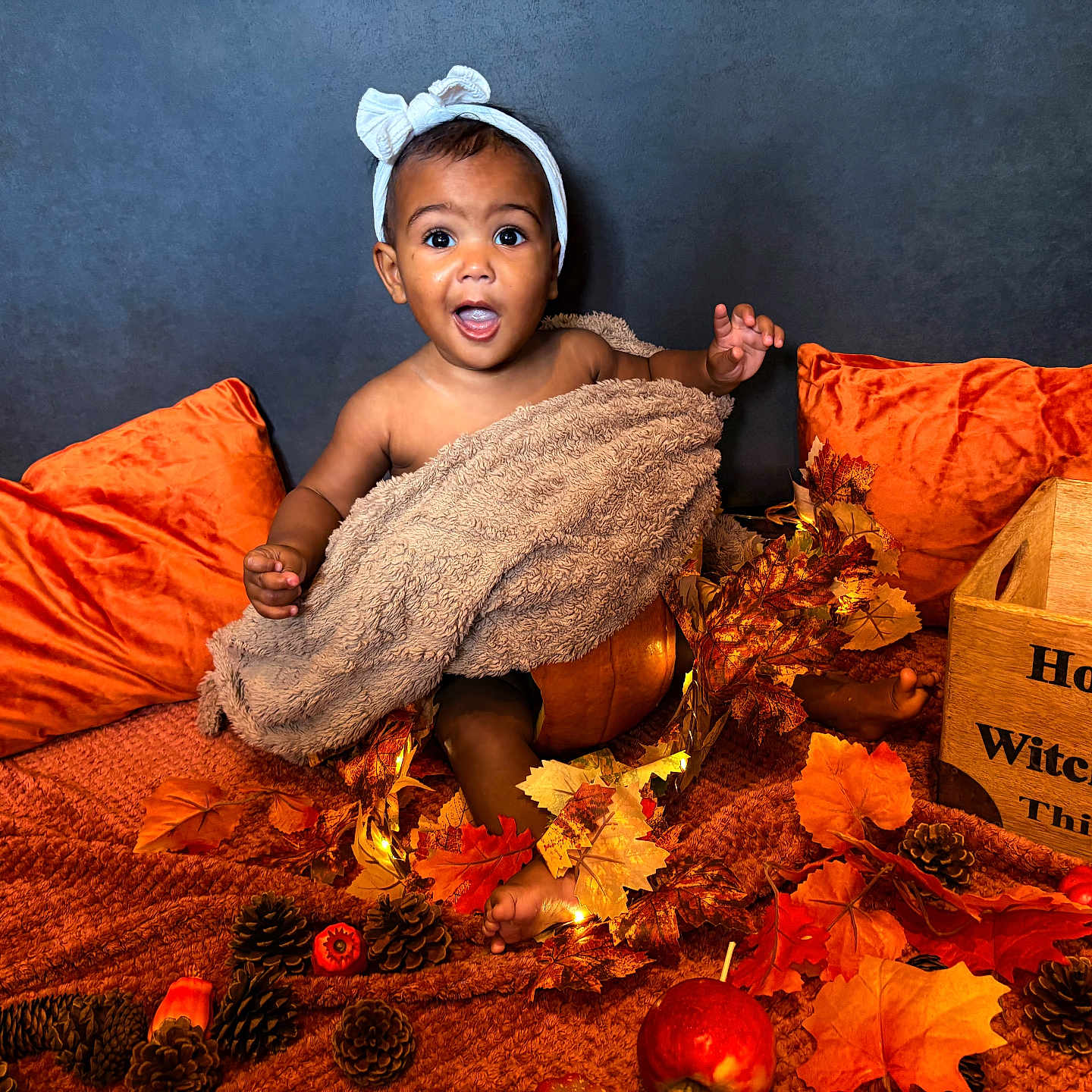 Trelawny is registered to the contest to win money with this photo: autumn_leaves, baby, blanket, child, cozy, cute, decorations, fall_decor, festive, happy, headband, indoor, orange_pillows, pinecones, portrait, pumpkin, seasonal, sitting, smiling, wooden_box