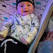 Noah joined the competition — help win amazing prizes! baby, infant, crib, beanie, hat, clothing, dollar_bill_pattern, hand, whale_pattern, bedding, smiling, person, cute, indoors, fabric, mesh, blanket, sleepwear, child, happy