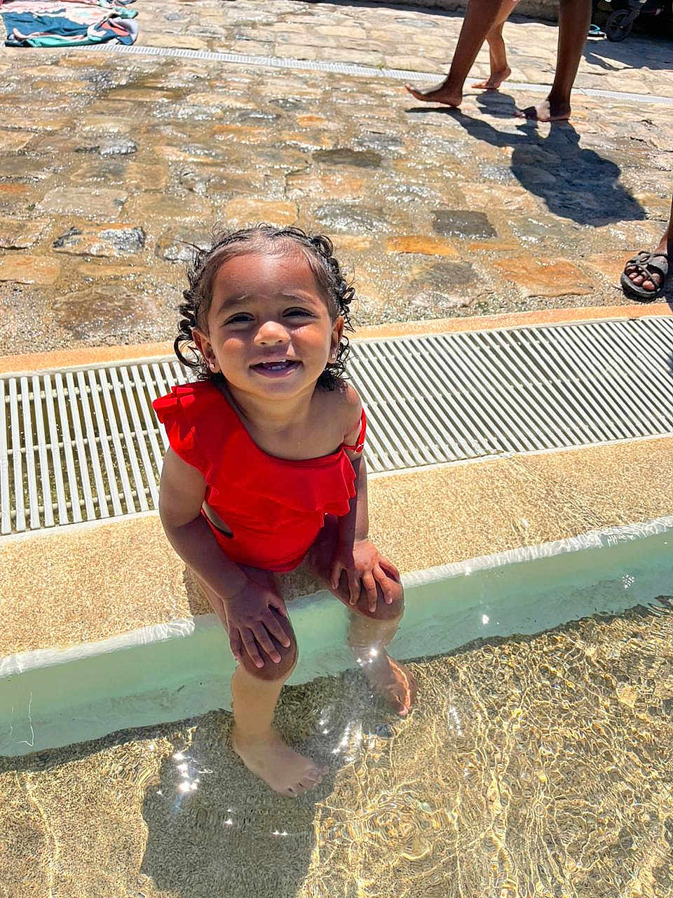 Shaelys participe au concours pour gagner de l'argent avec cette photo : toddler, child, swimsuit, red_clothing, water, pool, sitting, sunlight, outdoor, stone_pavement, feet, smiling, happy, summer, sunny, person, playing, vacation, reflection, shallow_water