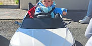 Samia a rejoint le concours — aidez-le/la à gagner de superbes lots ! baby, child, toy_car, audi, e_tron_sportback, pacifier, blue_clothing, outdoor, sunlight, sidewalk, house, window, fence, asphalt, person, footwear, shadow, seatbelt, driving, cute