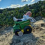 baby, toy, dump_truck, blanket, outdoor, sky, clouds, sand, hill, greenery, plants, child, infant, sunlight, nature, play, cute, wooden_sign, footwear, casual_clothing