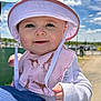 Clover is registered to the contest to win money with this photo: baby, child, hat, sun_hat, bib, giraffe_pattern, smiling, face, hand, outdoor, blue_sky, clouds, daylight, person, cute, infant, holding, clothing, closeup, happy