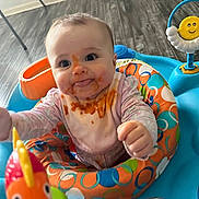 Clover is registered to the contest to win money with this photo: baby, child, messy_face, bib, activity_center, toy, fish_toy, colorful, indoor, floor, playtime, happy, cute, smiling, reaching, clothing, infant, seat, wooden_floor, face