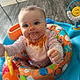 baby, child, messy_face, bib, activity_center, toy, fish_toy, colorful, indoor, floor, playtime, happy, cute, smiling, reaching, clothing, infant, seat, wooden_floor, face