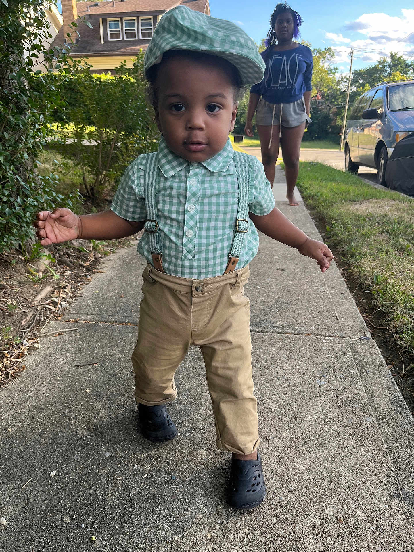 Daxon Dodds joined the competition — help win amazing prizes! toddler, child, sidewalk, green_checkered_cap, suspenders, khaki_pants, black_shoes, young_woman, barefoot, casual_clothing, suburban, grass, bushes, car, residential_area, summer, daylight, walking, outdoor, person