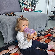 Loïs participe au concours pour gagner de l'argent avec cette photo : blue_eyes, bottle, casual_clothing, child, colorful, floor, home, indoor, lamp, long_sleeves, pillow, plant, pony_tail, relaxed, rug, sitting, socks, sofa, toddler, toy