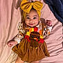 baby, infant, child, smile, bow_headband, yellow_bow, turkey_applique, dress, lying_down, bed, blanket, pink_sheet, brown_clothing, big_eyes, cheeks, hands, portrait, cute, happy, indoor