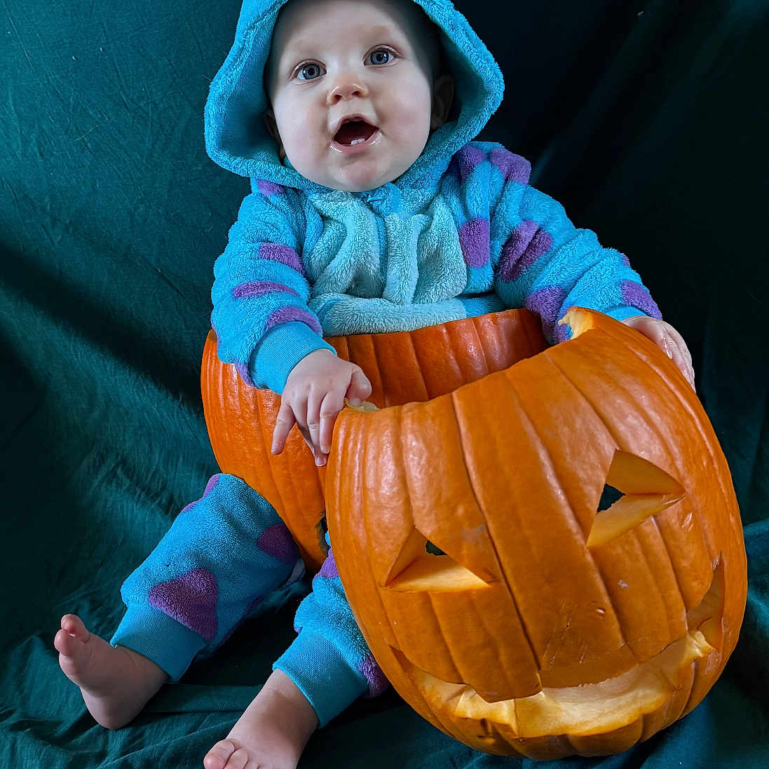 Hillarya a rejoint le concours — aidez-le/la à gagner de superbes lots ! baby, barefoot, blue, carved_pumpkin, child, costume, cute, dark_background, fabric, face, festive, halloween, holiday, indoors, onesie, portrait, pumpkin, purple, sitting, smiling