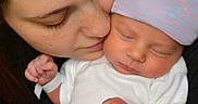 Samuel is registered to the contest to win money with this photo: baby, newborn, infant, mother, woman, face, sleeping, hat, striped_hat, white_clothing, skin, closeup, affection, love, family, holding, peaceful, portrait, indoor, tender