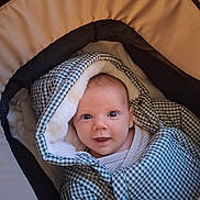 Basile a rejoint le concours — aidez-le/la à gagner de superbes lots ! baby, car_seat, checkered_pattern, child, clothing, cozy, cushion, cute, face, head, hood, indoor, infant, jacket, portrait, smiling, stroller, warm_clothing, wrapped, young_child