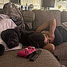 Athena is registered to the contest to win money with this photo: dog, black_dog, person, sleeping, cuddling, couch, living_room, indoors, home, blanket, pillow, television, remote_control, game_controller, gaming, relaxing, nap, pet, furniture, kitchen