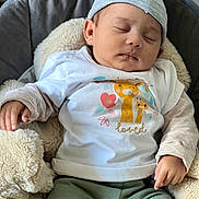 Thess participe au concours pour gagner de l'argent avec cette photo : baby, sleeping, infant, hat, white_shirt, giraffe_print, green_pants, blanket, soft_toy, cozy, cute, peaceful, child, portrait, indoors, resting, adorable, clothing, headwear, newborn