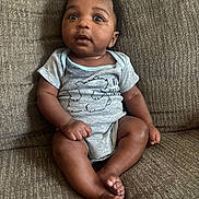 Symere joined the competition — help win amazing prizes! baby, child, infant, sitting, couch, onesie, clothing, face, expression, curious, indoors, brown, texture, furniture, person, portrait, skin, feet, hands, cute