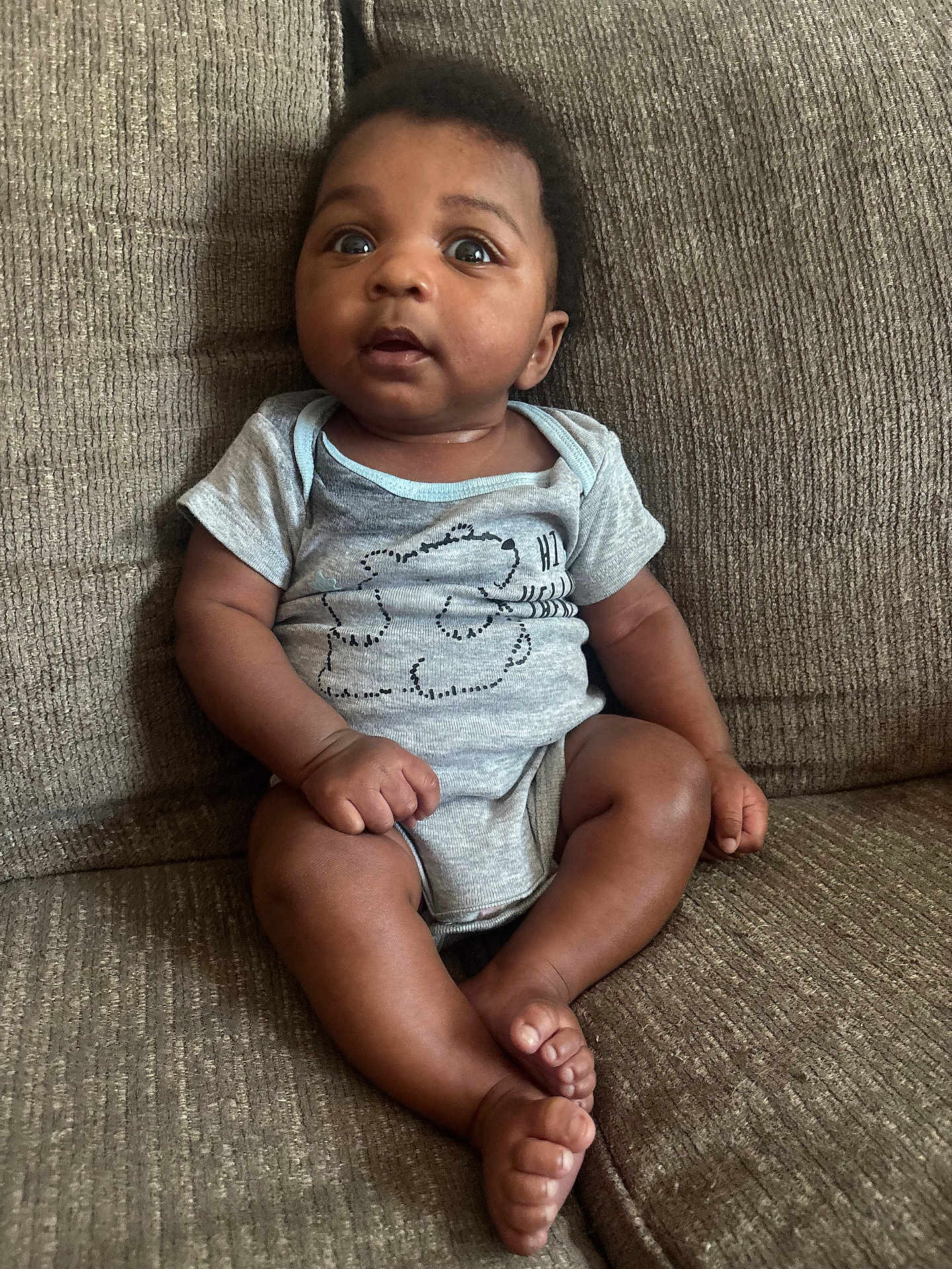 Symere joined the competition — help win amazing prizes! baby, child, infant, sitting, couch, onesie, clothing, face, expression, curious, indoors, brown, texture, furniture, person, portrait, skin, feet, hands, cute