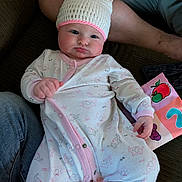 Lilith joined the competition — help win amazing prizes! adult, baby, bunny_ears, clothing, couch, cozy, cute, face, hand, hat, indoors, infant, knitted_hat, leg, onesie, pink, portrait, relaxed, soft_book, white