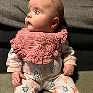 Aria joined the competition — help win amazing prizes! baby, child, pajamas, bib, pink_bib, carpet, sitting, curious, face, blue_eyes, indoor, cozy, soft_texture, cushion, yellow_pillow, woodland_pattern, infant, portrait, closeup, cute