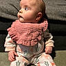 baby, child, pajamas, bib, pink_bib, carpet, sitting, curious, face, blue_eyes, indoor, cozy, soft_texture, cushion, yellow_pillow, woodland_pattern, infant, portrait, closeup, cute