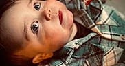 Xavier is registered to the contest to win money with this photo: toddler, child, face, eyes, leaf, hand, plaid_jacket, clothing, portrait, indoors, curious, autumn, warm_tones, soft_focus, close_up, skin, hair, expression, cozy, young_child