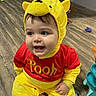 Xavier is registered to the contest to win money with this photo: toddler, child, costume, pooh_bear, yellow, red, happy, smiling, indoor, floor, wooden_floor, toy, playtime, baby, cute, face, headgear, clothing, sitting, person