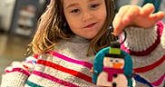 Leah joined the competition — help win amazing prizes! child, girl, sweater, striped_sweater, snowman, ornament, toy, indoor, home, blurred_background, hand, happy, smile, long_hair, casual_clothing, person, warm_lighting, cozy, decor, playful