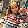 child, girl, sweater, striped_sweater, snowman, ornament, toy, indoor, home, blurred_background, hand, happy, smile, long_hair, casual_clothing, person, warm_lighting, cozy, decor, playful