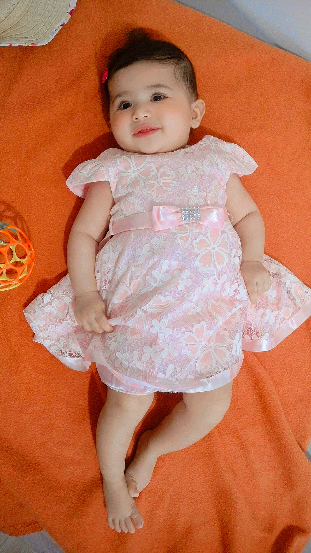Ella participe au concours pour gagner de l'argent avec cette photo : baby, baby_toddler_clothing, cheek, child, day_dress, dress, embellishment, finger, formal_wear, happy, iris, neck, one_piece_garment, pattern, peach, person, pink, skin, sleeve, smile