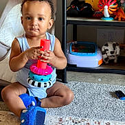 Azarius joined the competition — help win amazing prizes! toddler, child, toy, stacking_toy, indoor, carpet, sitting, blue_outfit, dinosaur_slippers, shelf, stuffed_animal, plush_toy, floor, home, play, cute, focused, person, baby, furniture