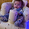 baby, infant, child, onesie, inflatable_chair, paper_towel, wood_paneling, indoor, seated, cushion, blue_clothing, pattern, curious, face, person, plush, cozy, soft_lighting, home_interior, expression
