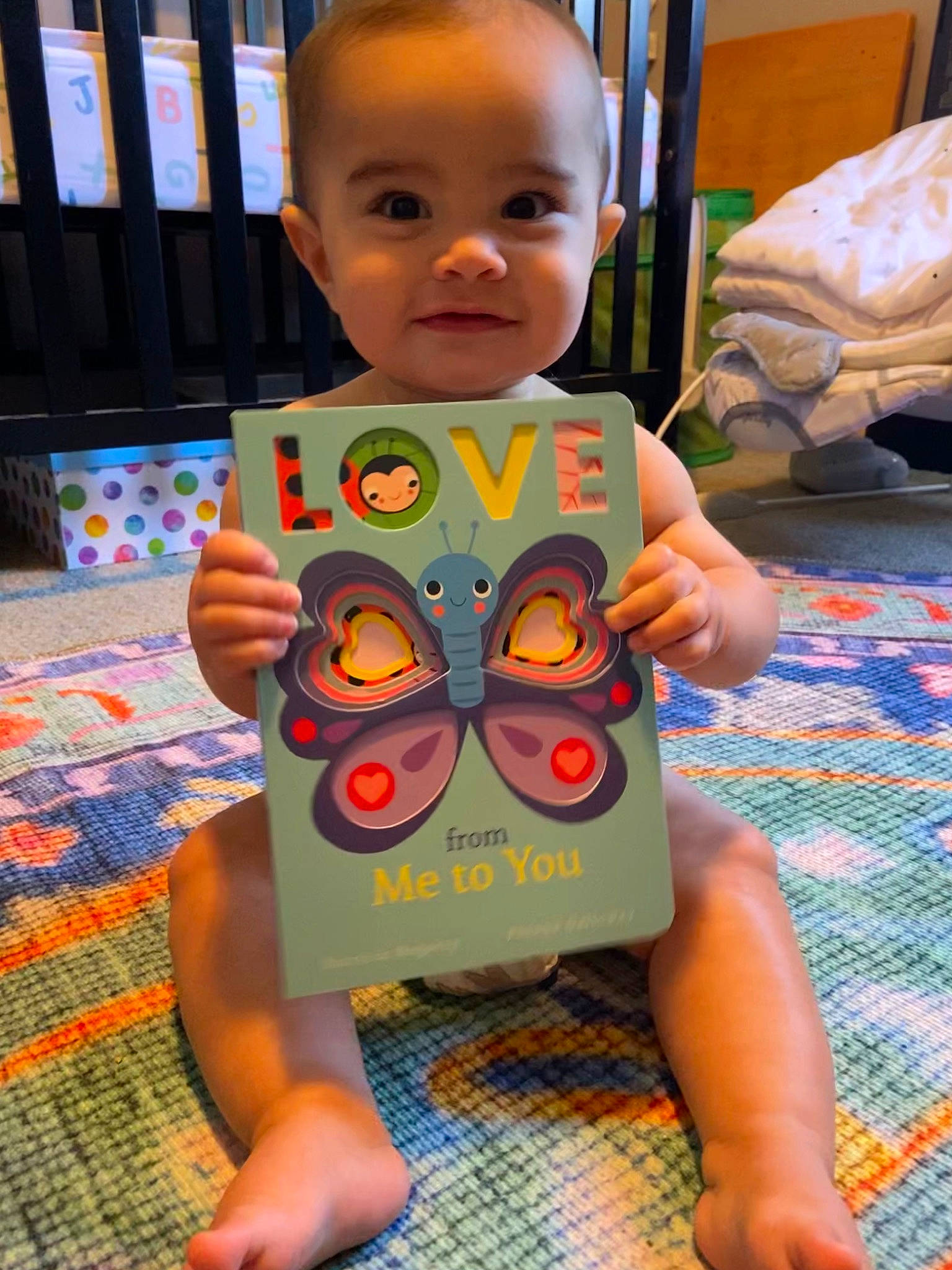 Indie is registered to the contest to win money with this photo: baby, baby_toddler_clothing, carmine, chest, child, comfort, eye, face, flooring, fun, head, human_body, iris, joy, linens, pattern, person, play, room, sitting