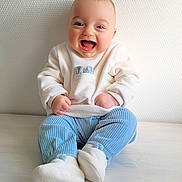 Eliott participe au concours pour gagner de l'argent avec cette photo : baby, smiling, child, sitting, blue_pants, white_sweater, indoor, floor, happy, cute, portrait, infant, warm_clothing, soft_texture, footwear, light, expression, face, hands, casual