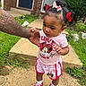 Jalena is registered to the contest to win money with this photo: toddler, child, person, sidewalk, grass, outdoor, red_shoes, minnie_mouse, shorts, tshirt, hair_bows, tattoo, adult_hand, curious_expression, concrete, greenery, summer_clothing, walking, cute, support