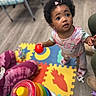 Jalena is registered to the contest to win money with this photo: toddler, child, indoor, toy, colorful, puzzle_mat, ball, curly_hair, pink_clothing, play, floor, person, footwear, cute, expression, childhood, playtime, home, happy, young