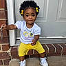 toddler, child, curly_hair, yellow_bows, white_tshirt, yellow_shorts, sneakers, brick, doorstep, chain, smile, outdoor, portrait, cute, sitting, accessory, happy, person, casual_clothing, daylight
