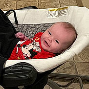 Violet is registered to the contest to win money with this photo: baby, infant, smile, red_shirt, mickey_mouse, baby_rocker, indoor, floor_tiles, happy, child, cute, person, young, clothing, seat, head, face, relaxing, home, comfort