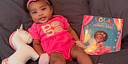 Aurora is registered to the contest to win money with this photo: baby, child, girl, pink_clothing, headband, bow, unicorn_toy, book, couch, smile, cute, infant, indoors, portrait, sitting, toy, face, happy, childrens_book, soft_lighting