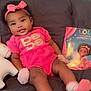 baby, child, girl, pink_clothing, headband, bow, unicorn_toy, book, couch, smile, cute, infant, indoors, portrait, sitting, toy, face, happy, childrens_book, soft_lighting