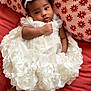 Aurora joined the competition — help win amazing prizes! baby, infant, dress, white_dress, flower_headband, socks, floral_pattern, pillow, bed, couch, cute, portrait, child, indoor, soft_lighting, smiling, toddler, cozy, sleepwear, resting