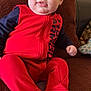 baby, child, red_onesie, couch, indoor, blue_eyes, face, tongue_out, sitting, furniture, plush, casual, comfort, portrait, infant, person, home, cute, smiling, relaxed