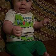 Kenneth is registered to the contest to win money with this photo: baby, child, indoor, couch, patterned_couch, green_pants, buzz_lightyear_shirt, barefoot, sitting, portrait, face, expression, young_child, furniture, person, cute, hands, feet, wide_eyes, casual_clothing