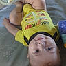 Remington is registered to the contest to win money with this photo: baby, child, smiling, yellow_shirt, toy, playmat, elephant_pattern, curly_hair, lying_down, indoors, cute, infant, soft_surface, colorful, happy, person, portrait, young_child, baby_toys, casual_clothing