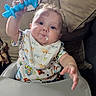 Remington is registered to the contest to win money with this photo: baby, high_chair, teething_toy, bib, messy_face, indoor, cushion, sofa, child, infant, blue_toy, clothing, hand, face, expression, furniture, cute, young_child, feeding_time, happy