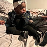 baby, child, headband, denim_jacket, black_clothing, sneakers, bed, blanket, pillow, indoor, cute, portrait, sitting, curious, young_child, fashion, cozy, soft_lighting, infant, expression