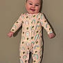 baby, child, pajamas, rainbow_pattern, dog_pattern, smiling, standing, indoors, face, cute, happy, onesie, footed_pajamas, infant, person, clothing, wall, skin, head, expression