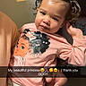 child, toddler, pink_shirt, cartoon_graphic, pigtails, curly_hair, indoor, adult_hand, holding, expression, face, person, sitting, portrait, casual_clothing, snapchat_overlay, text_overlay, family, love, thankful