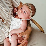 Lily Rose a rejoint le concours — aidez-le/la à gagner de superbes lots ! baby, infant, child, person, human, tattoo, hand, arm, flower_crown, white_clothing, knitwear, skin, cute, cute_baby, holding, portrait, indoor, soft_light, neutral_background, tender_moment