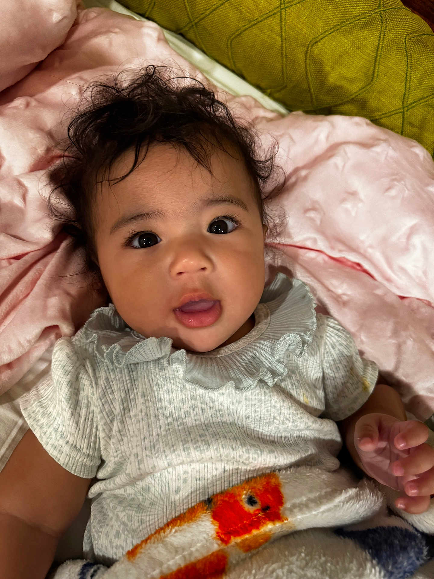 Nevaeh is registered to the contest to win money with this photo: baby, infant, child, blanket, cushion, pink, green, curly_hair, face, eyes, mouth, clothing, soft_texture, indoor, portrait, cute, lying_down, hand, expression, comfortable